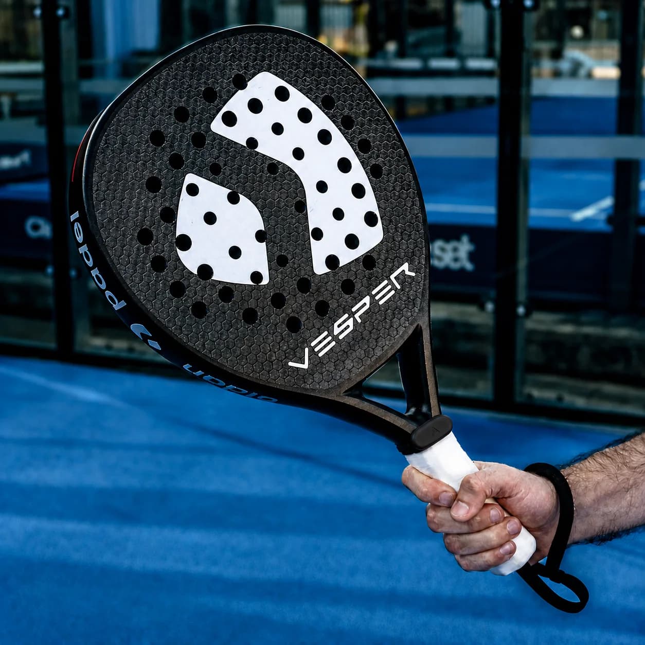 Aurevo pod clipped to the handle of a padel racket held up on a padel court