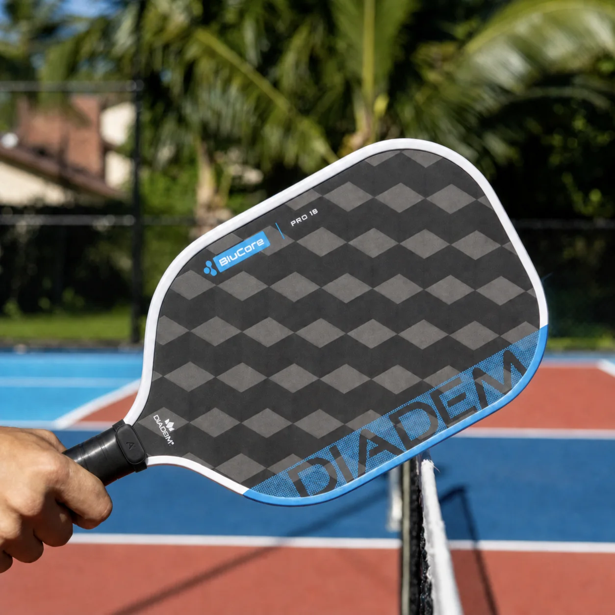 Aurevo pod clipped to the handle of a pickleball paddle held above the net